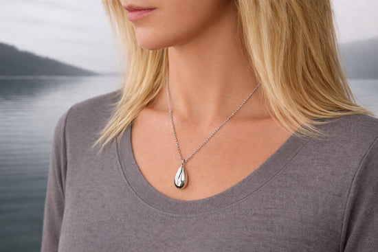 Collier pendentif goutte commémoratif porté au cou dans un univers sobre et apaisant au bord d’un lac