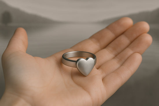 Bague cœur commémorative posée dans une main dans un univers sobre et apaisant