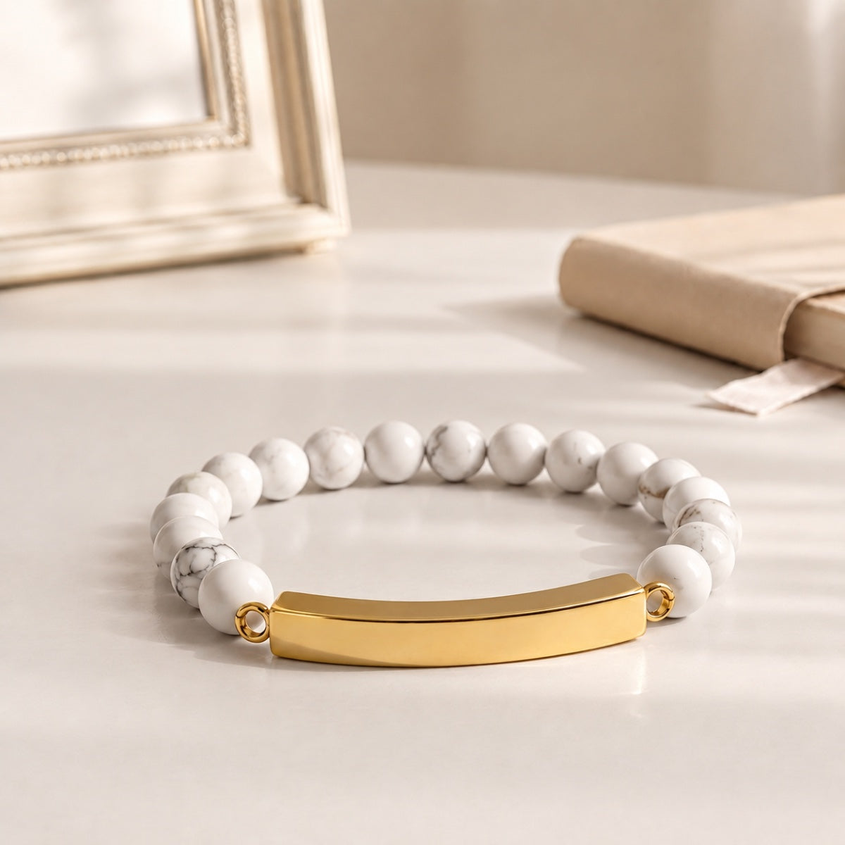 Bracelet pierre du souvenir blanc metal-jaune avec perles effet marbre blanc et barre présenté dans une ambiance intérieure raffinée
