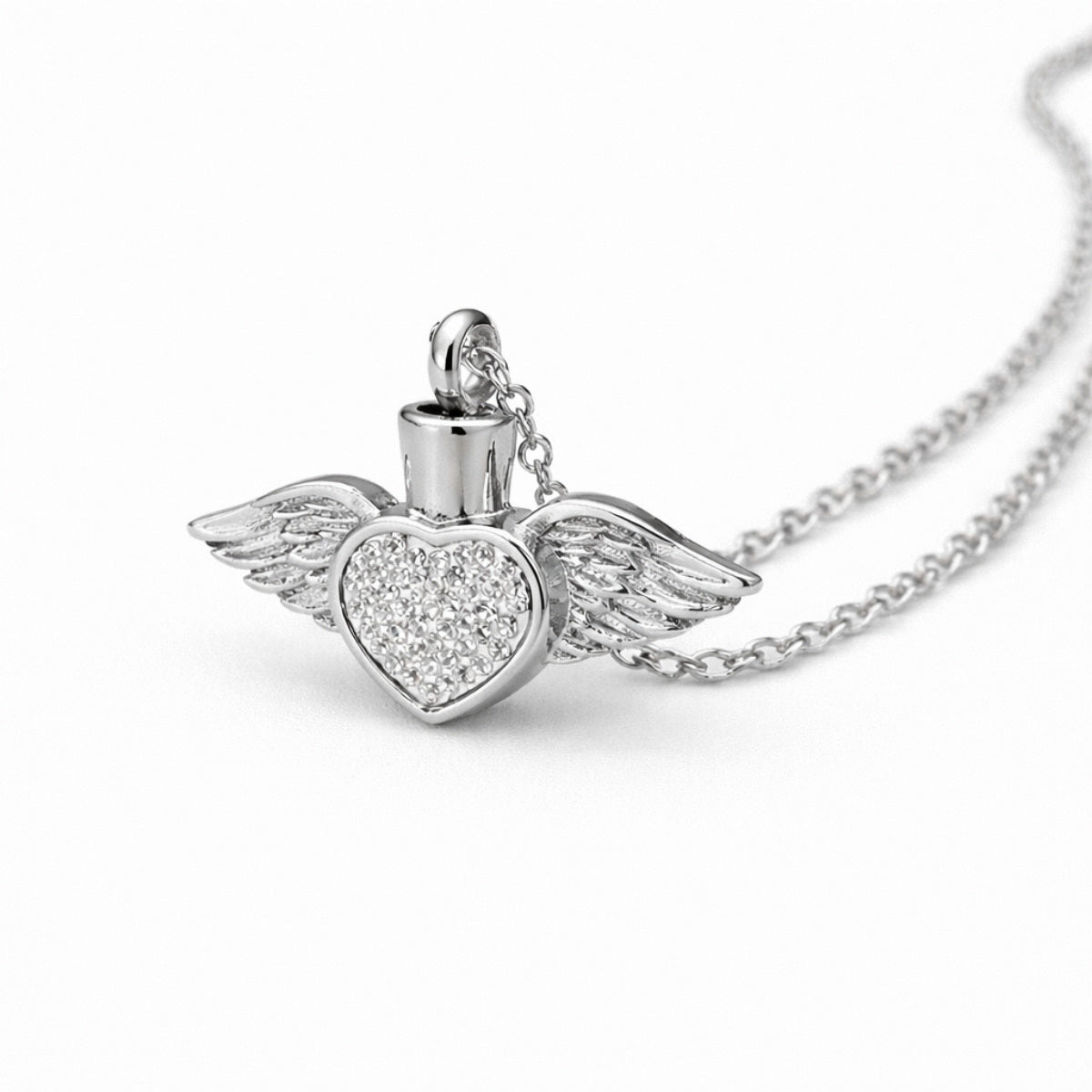 Vue 3/4 du collier cœur ailé urne en acier inoxydable argenté mettant en valeur ses ailes et son compartiment intégré